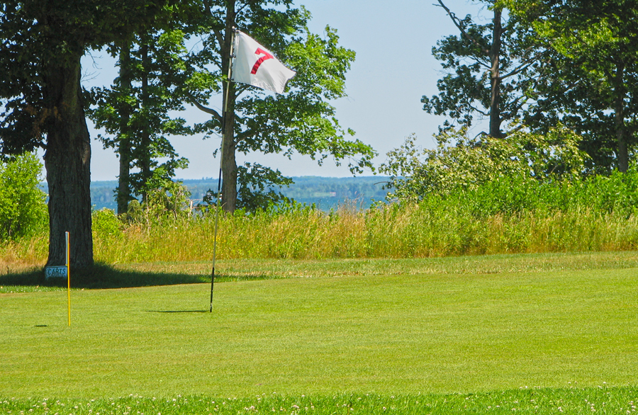 Hole 2 green at Nahma Golf Club with the bay on the horizon.